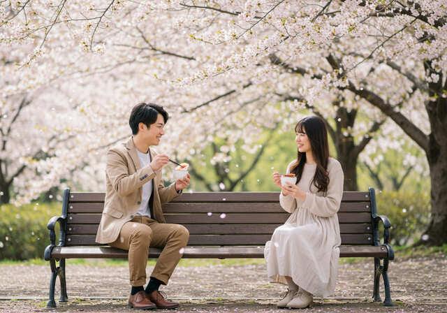 桜の舞う公園で弁当を食べる男女